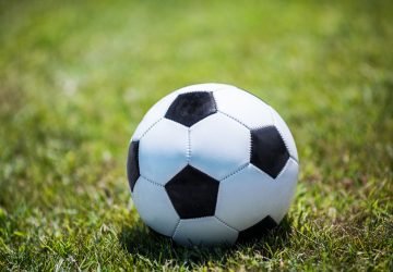 Traditional football shining in the sun on green field. Soccer is the most popular team game all over the world