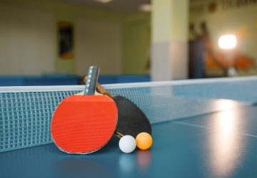Two ping pong paddles on the table with net, nobody, closeup view. Table-tennis club, tennis concept